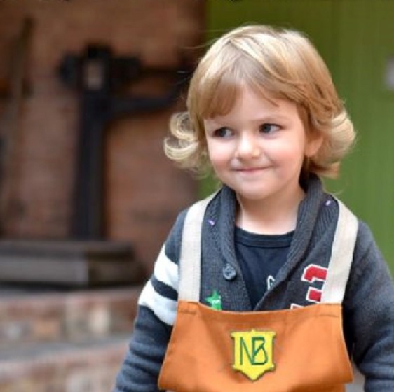 Young boy smiling, he is wearing a brown apron with the Newman Brothers logo on it