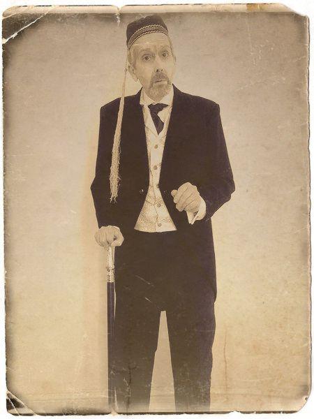 faded aged image of smartly dressed man wearing a smoking cap and leaning on a cane