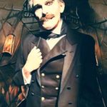 Man with moustache in suit stands in front of haunted house background