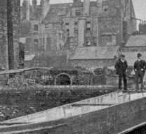 black and white newspaper image. two men stare down at a barge sitting in ruins