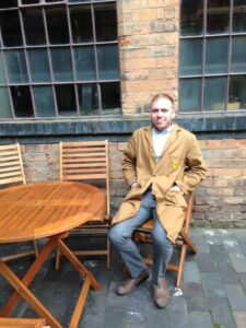 Photo of volunteer in brown coat sitting at a table in the courtyard