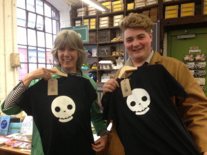 Two volunteers each hold up a black tshirt with a skull in front of themselves. 