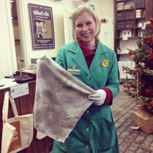 Vicki, wearing a green overall and smiling at the camera wears protective gloves and holds a Cleaning cloth