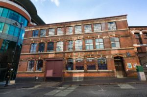 Exterior of the Newman Brothers Factory. Red brick building with large red gates and many leaded windows over 3 floors.