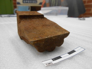 Rusty object next to a piece of paper on a white surface