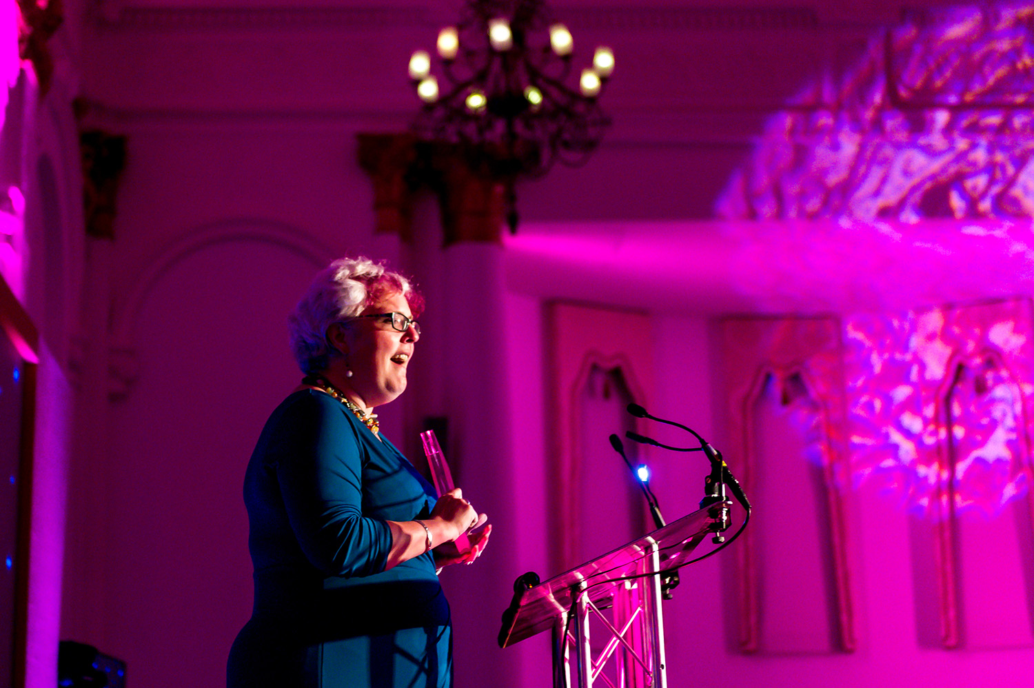 Jenni speaking at the dais in a hall lit by purple light