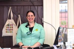 Kerry standing behind the reception desk, wearing a green overall