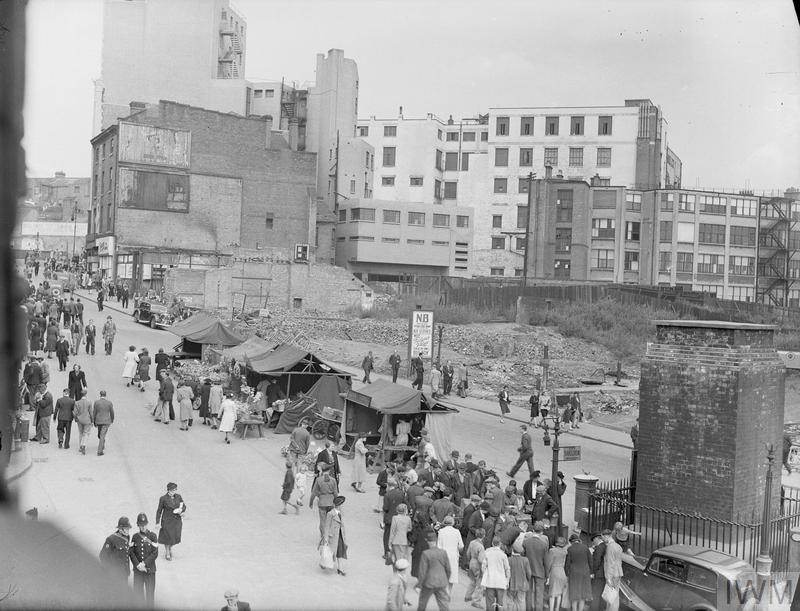 Just three years previous. Bull Ring, Birmingham 1942. Men and women shop amongst the market stalls that line the centre of the road in Birmingham's bomb-damaged Bull Ring Market Square. Rubble and the exterior walls, which can be seen in the background of the photograph, are all that remains of the old market. 
