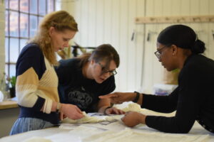 Three people stand around a table pointing at illustrations