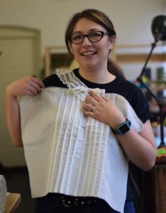 A woman holds up part of a shroud against her torso demonstrating a "fit"