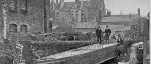 black and white newspaper image. two men stare down at a barge sitting in ruins