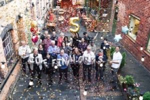 Group of volunteers celebrate in courtyard with balloons and streamers.