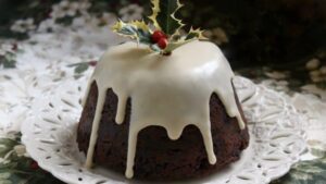 Christmas pudding with cream with sauce of some kind poured on it. a sprig of holly on top