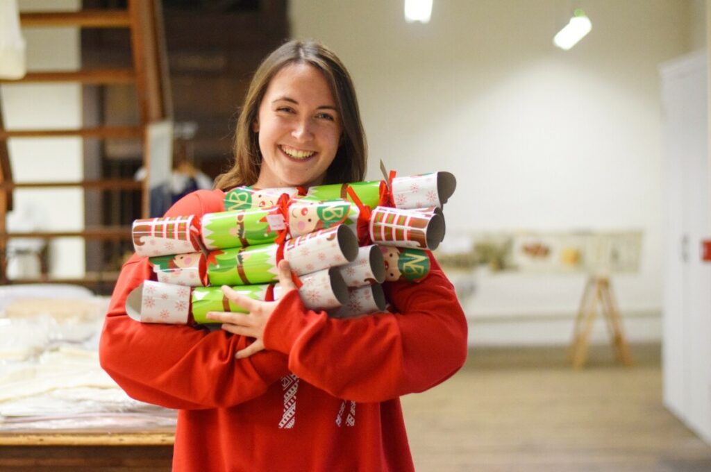 Woman in red jumper has arms full of large christmas crackers.