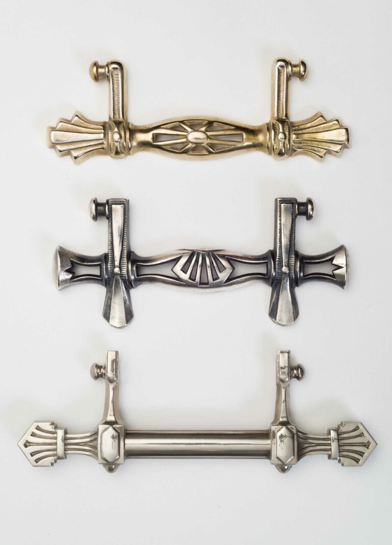 Three art deco coffin handles. top one is brass. middle is thick and a dark silver colour. the bottom is the longest and a lighter silver colour