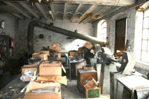 Polishing Shop pre restoration, lots of open cardboard boxes and metal machinery in a brick walled room