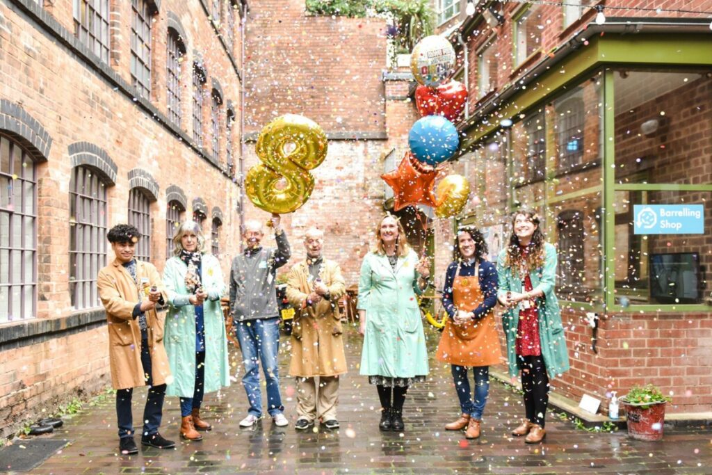 Coffin works volunteers in the courtyard holding helium filled balloons, celebrating. one ballon is golden and in the shape of and eight