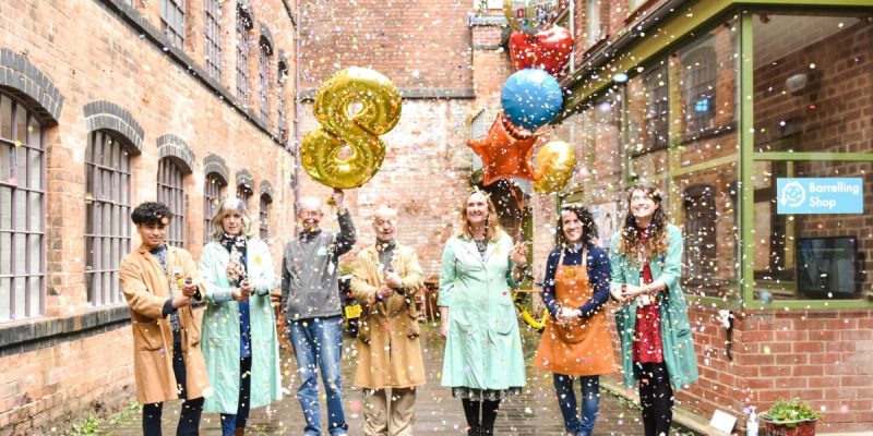Coffin works volunteers in the courtyard holding helium filled balloons, celebrating. one ballon is golden and in the shape of and eight