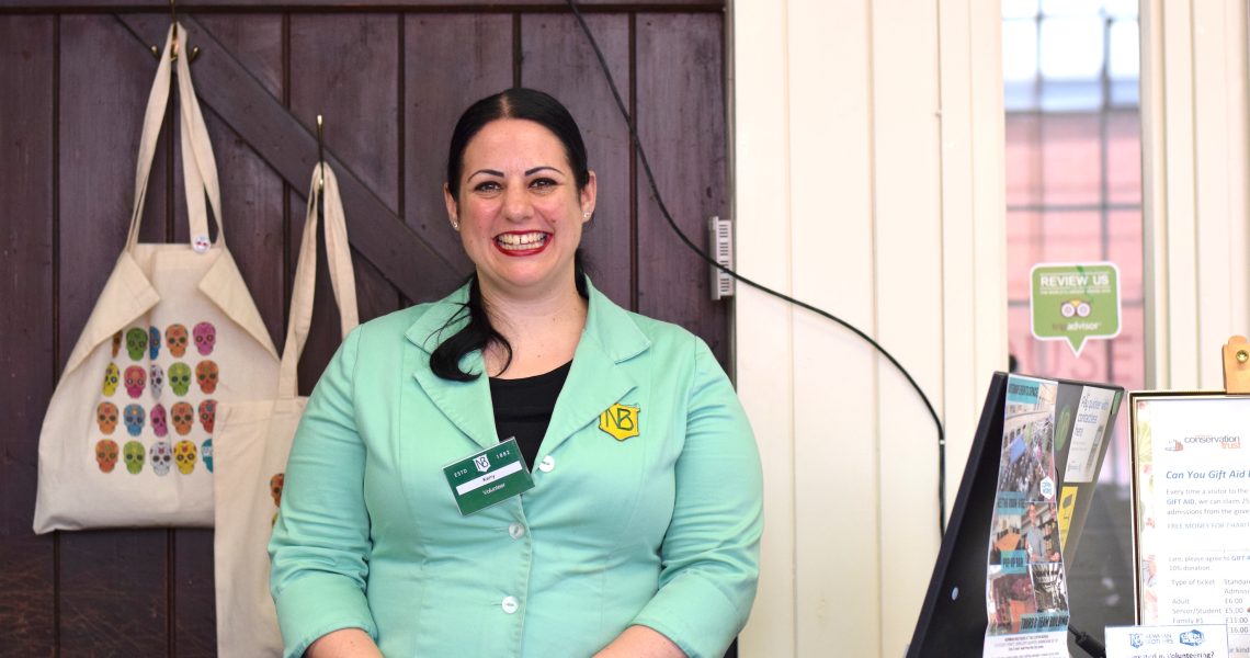 Kerry standing behind the reception desk, wearing a green overall