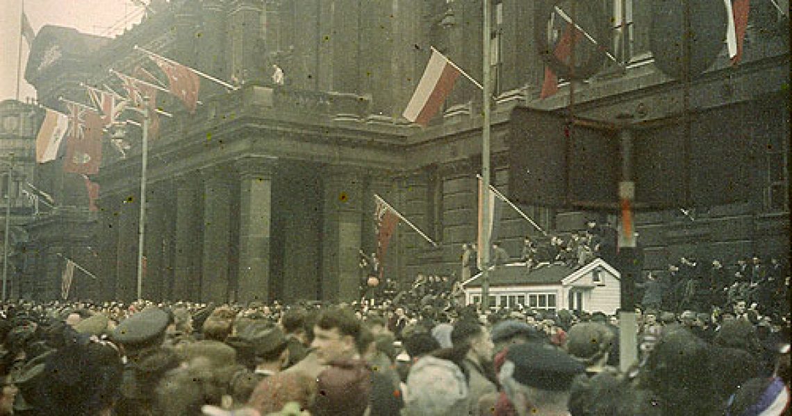A crowd stands in front of the Council House for VE Day Celebrations, May 1945. There are world flags on display.