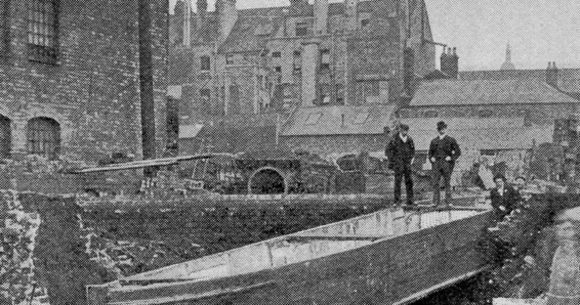 black and white newspaper image. two men stare down at a barge sitting in ruins