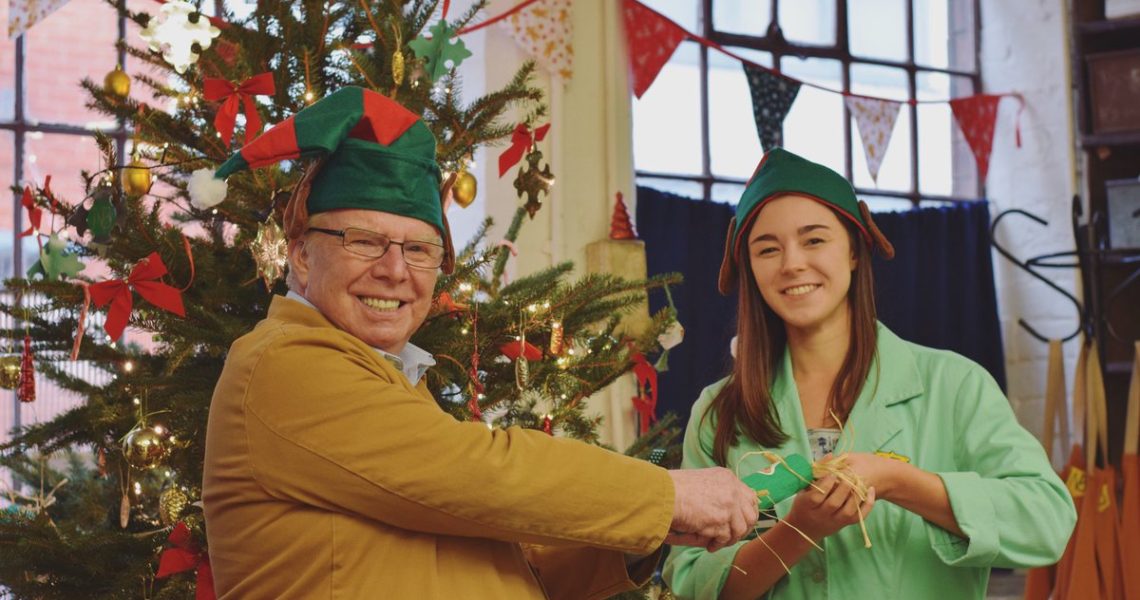 Two volunteers pull a christmas crackers staning in front of a christmas tree