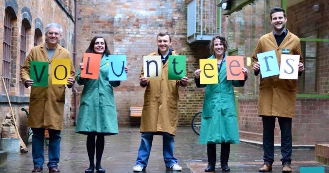 Volunteers stand in a row, holding up coloured sheets of paper spelling out the word "volunteers".